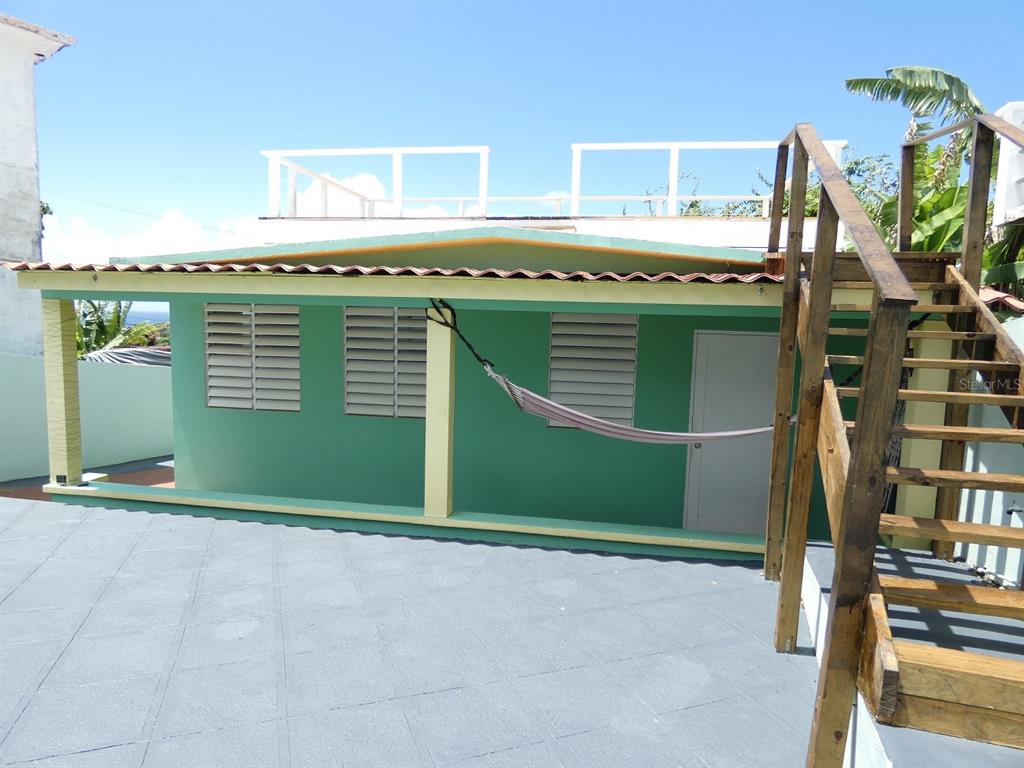 A green exterior wall with louvered windows, a hammock, and wooden stairs leading to a roof — E115 CALLE M-GARCIA, VIEQUES, PR