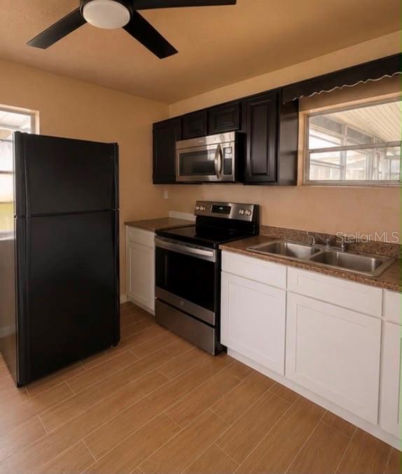 A kitchen features black upper cabinets, white lower cabinets, stainless steel appliances, and wood-look flooring — 1718 KENTUCKY AVENUE, ST CLOUD, FL