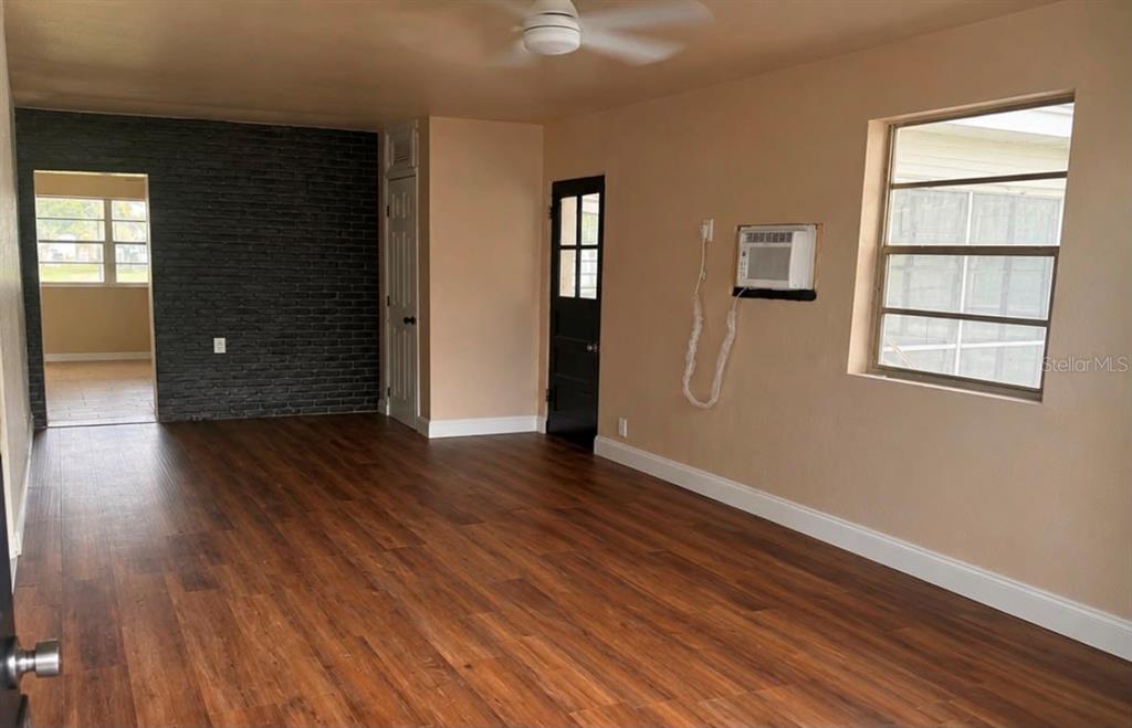 A living room with wood-look flooring, a dark brick accent wall, and a window unit — 1718 KENTUCKY AVENUE, ST CLOUD, FL