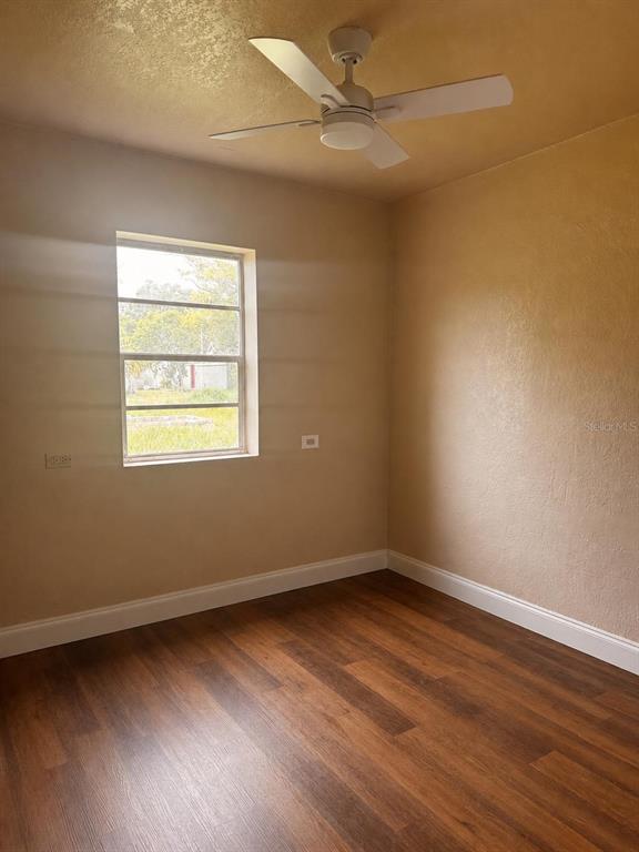 An empty bedroom features wood-look flooring, a ceiling fan, and a window overlooking a yard — 1718 KENTUCKY AVENUE, ST CLOUD, FL