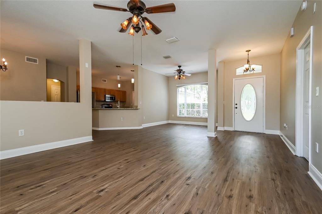 An open-concept living area features wood-look flooring, two ceiling fans, and an adjacent kitchen — 2221 MOUNTAIN MEADOW WAY, VALRICO, FL