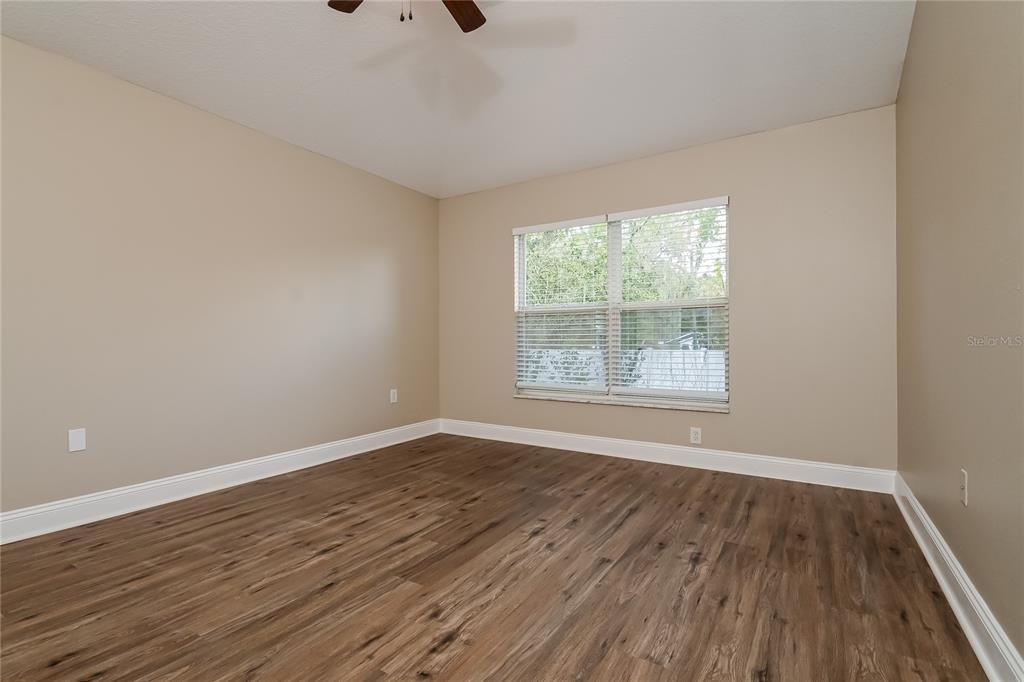 An empty bedroom features beige walls, wood-look flooring, and a window with white blinds — 2221 MOUNTAIN MEADOW WAY, VALRICO, FL
