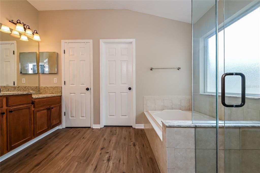 A bathroom features wood-look flooring, a wooden vanity, a soaking tub, and a glass shower — 2221 MOUNTAIN MEADOW WAY, VALRICO, FL
