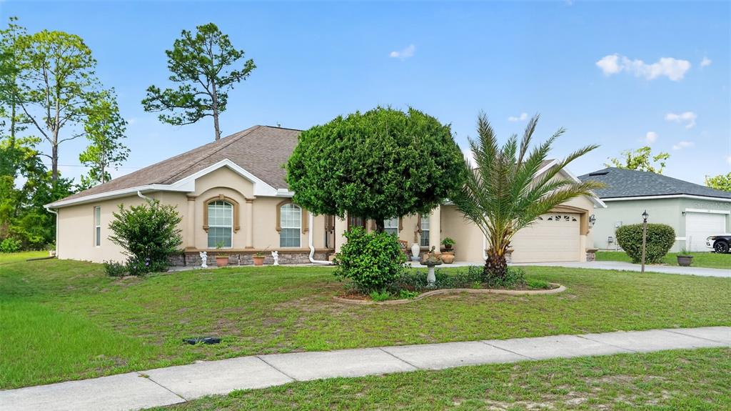A single-story tan house with a palm tree and a manicured bush in the front yard — 208 MARION OAKS TRAIL, OCALA, FL