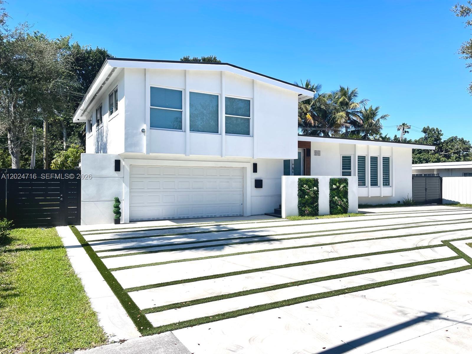 A two-story white house features a modern driveway with grass strips and vertical wall planters — 19960 Highland Lakes Blvd, Miami FL 33179, MIAMI, FL