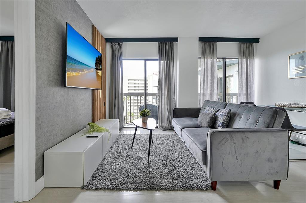 A modern living room features a grey sofa, a wall-mounted television, and floor-to-ceiling curtains — 6165 CARRIER DRIVE UNIT 3701, ORLANDO, FL