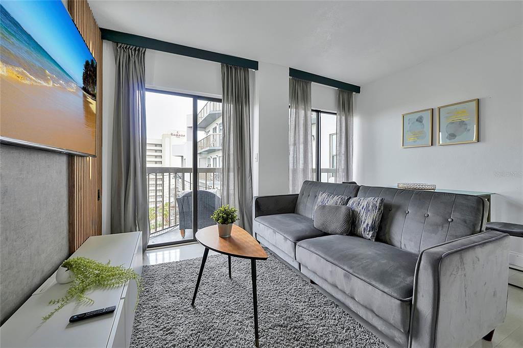 A living room features a gray sofa, a wooden coffee table, and a wall-mounted television — 6165 CARRIER DRIVE UNIT 3701, ORLANDO, FL