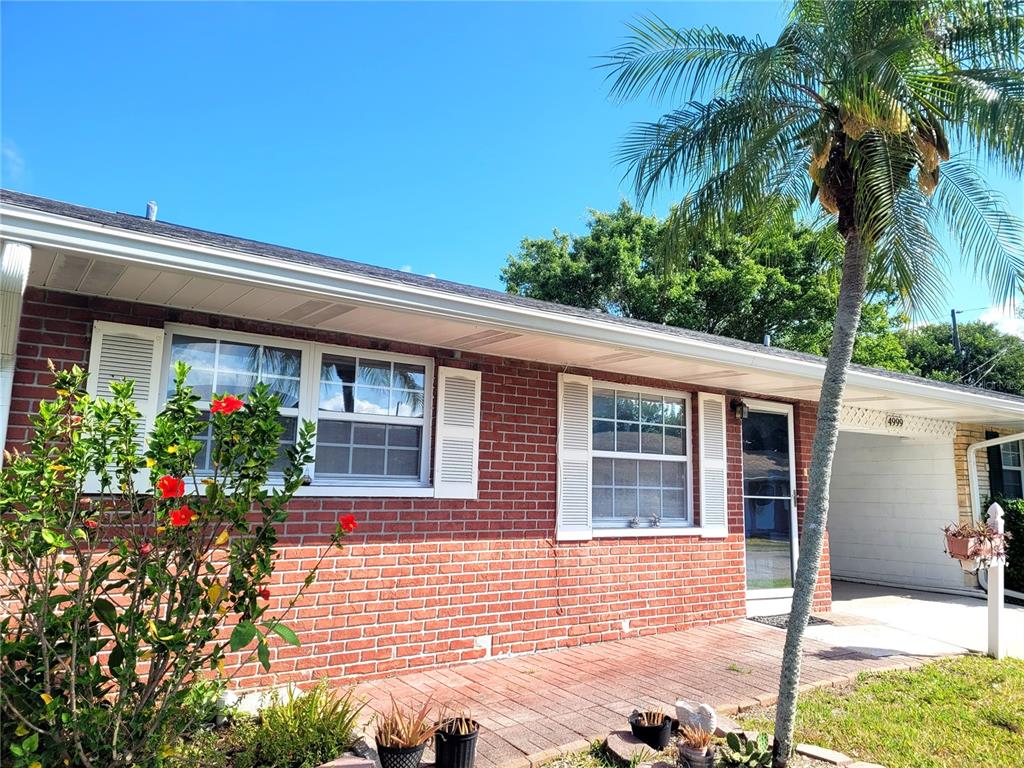 A brick house exterior features a front patio, white shutters, and a palm tree — 4999 SPRINGWOOD COURT, PINELLAS PARK, FL