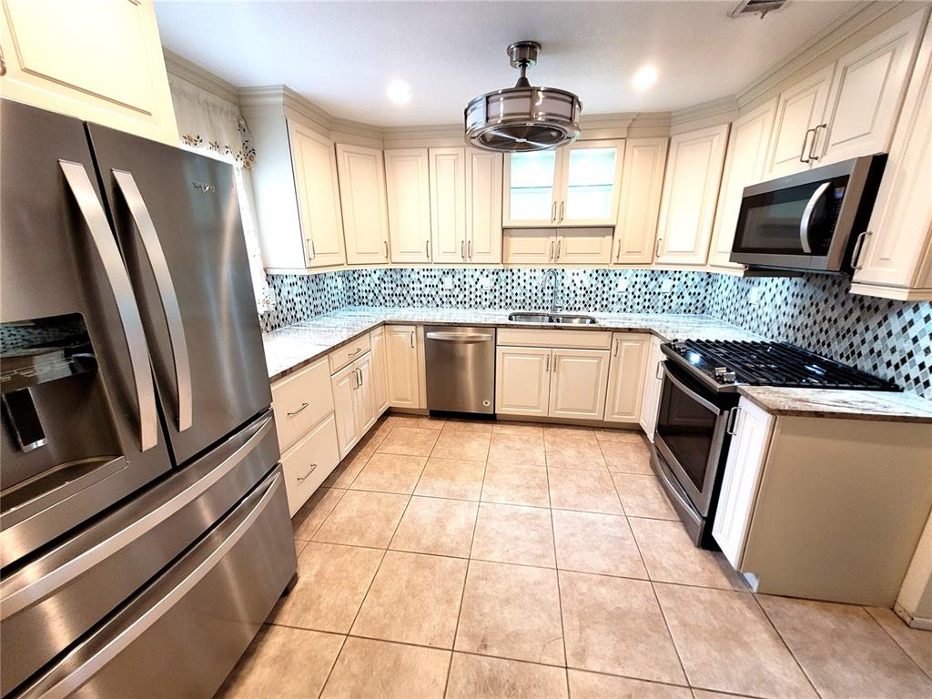 A kitchen features stainless steel appliances, off-white cabinetry, a patterned backsplash, and tile flooring — 4999 SPRINGWOOD COURT, PINELLAS PARK, FL