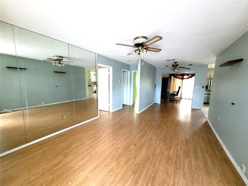 A living room with light wood-look flooring, a mirrored wall, and two ceiling fans — 4999 SPRINGWOOD COURT, PINELLAS PARK, FL