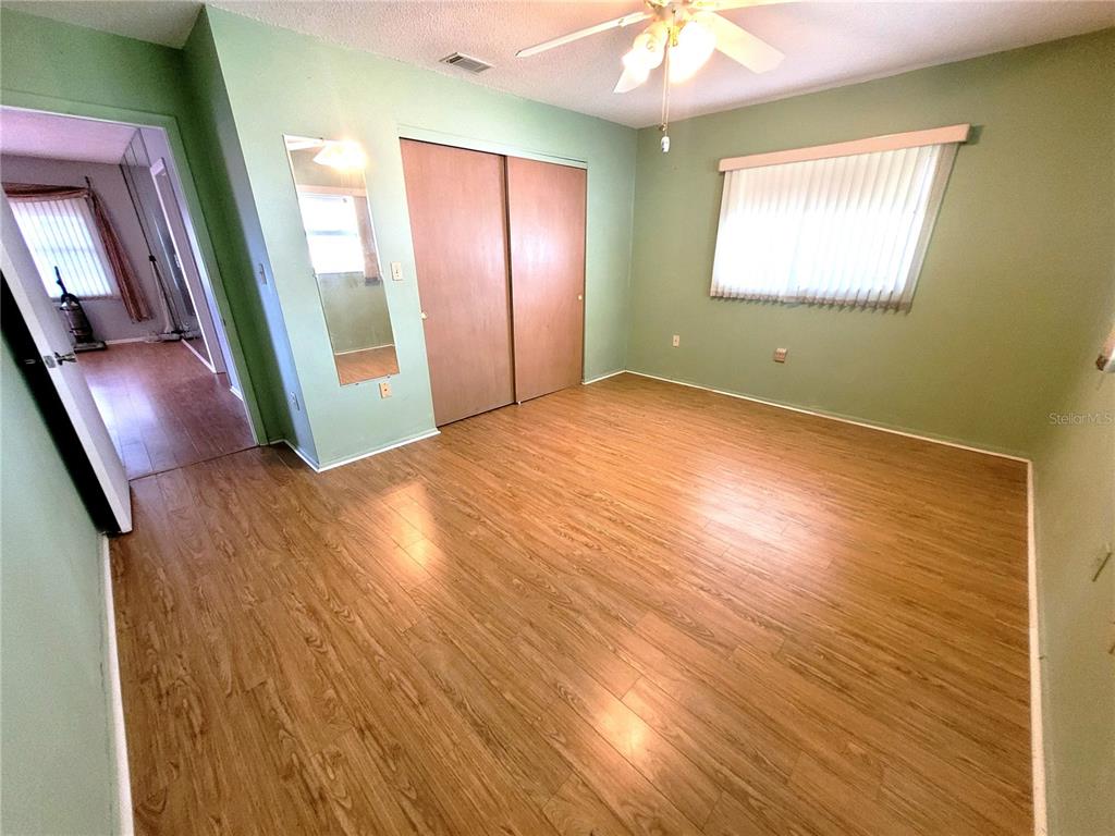 A bedroom with light green walls, wood-look flooring, a ceiling fan, and sliding closet doors — 4999 SPRINGWOOD COURT, PINELLAS PARK, FL