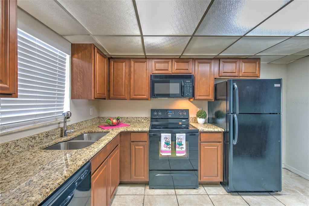 A kitchen features wood cabinets, granite countertops, black appliances, and a drop ceiling — 711 RUSSELL LANE UNIT 134, BRANDON, FL