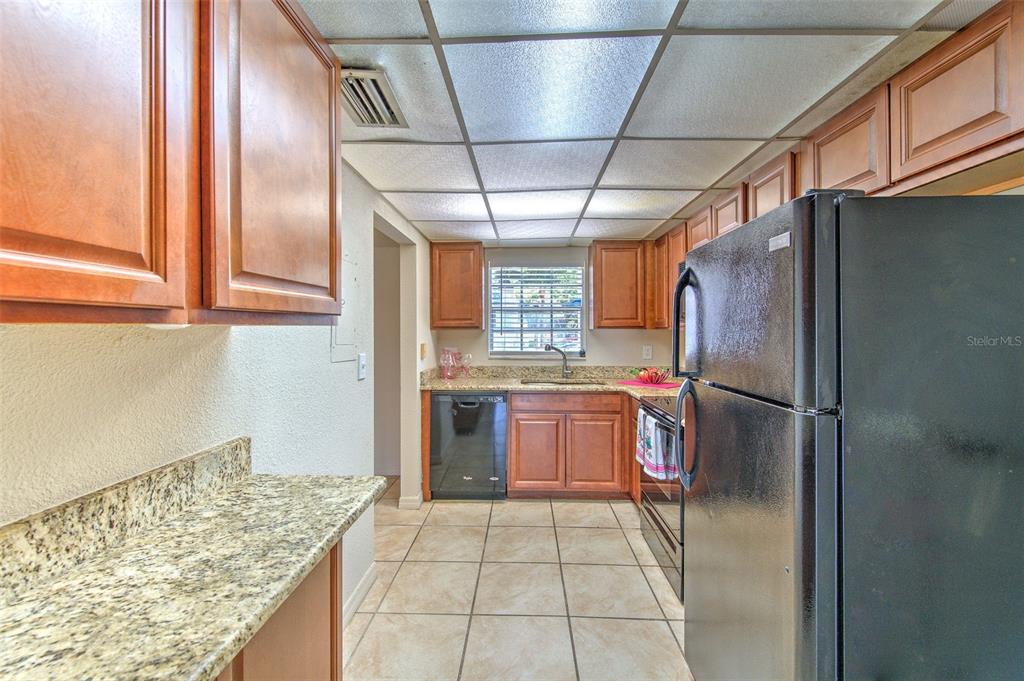 A galley kitchen features wood cabinets, granite countertops, tile flooring, and black appliances — 711 RUSSELL LANE UNIT 134, BRANDON, FL