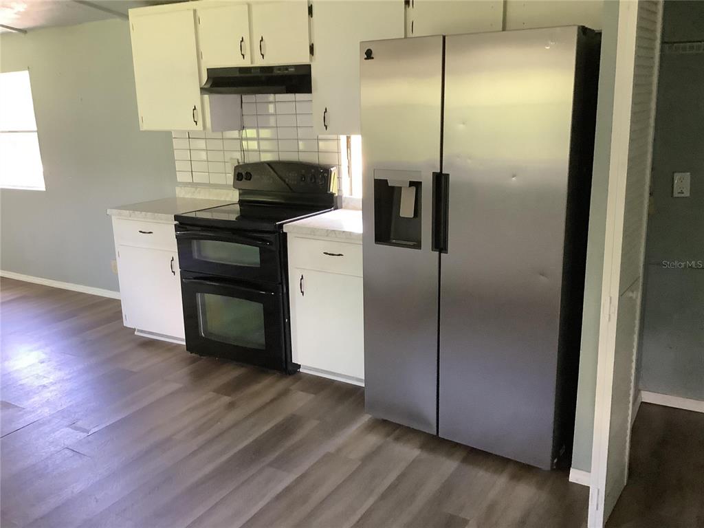 A kitchen features white cabinets, a black double oven, and a stainless steel refrigerator — 13585 SE 119TH STREET, OCKLAWAHA, FL