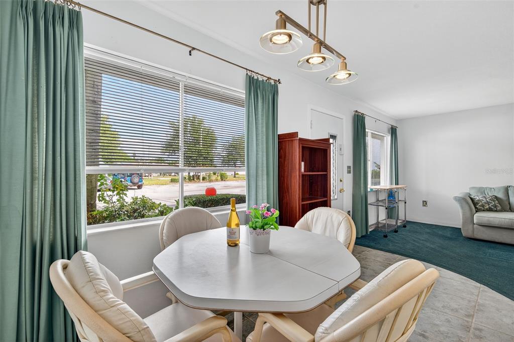 A dining area features a white table, four chairs, and a large window with curtains — 11100 86TH AVENUE UNIT 108, SEMINOLE, FL
