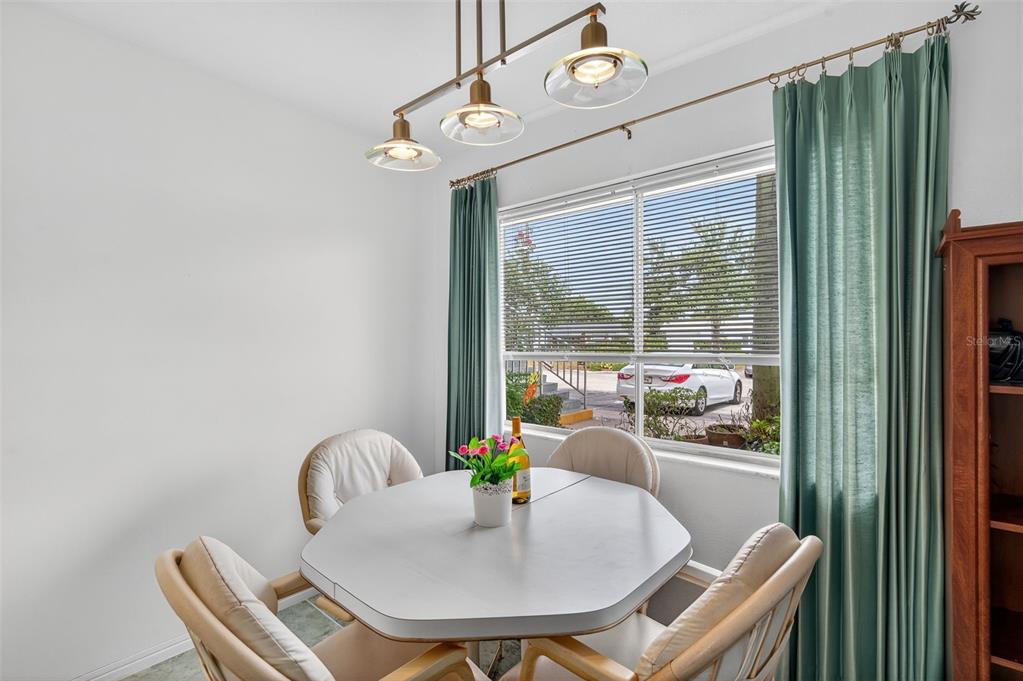 A dining area features a white table, four chairs, a pendant light, and green curtains — 11100 86TH AVENUE UNIT 108, SEMINOLE, FL