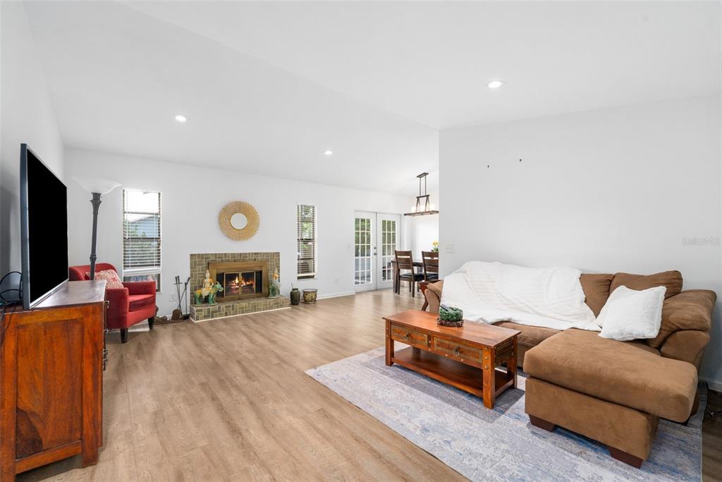A living room with light wood flooring, a fireplace, a brown sectional, and a television — 8127 SW 12TH PLACE, GAINESVILLE, FL
