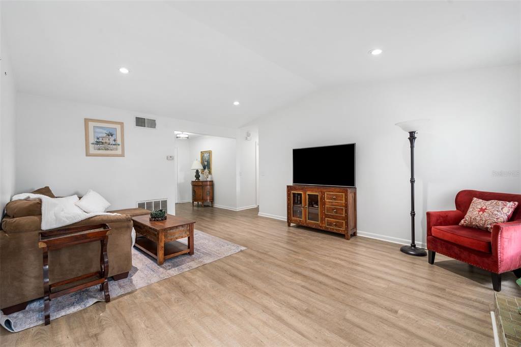A living room features light wood-look flooring, a brown sectional sofa, and a red armchair — 8127 SW 12TH PLACE, GAINESVILLE, FL