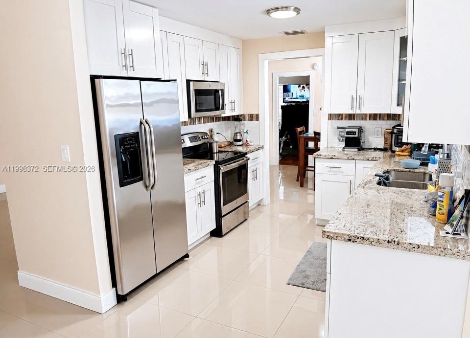 A kitchen features white cabinets, stainless steel appliances, and granite countertops with light tile flooring — 146 BONFIRE, Palm Bay FL 32907, PALM BAY, FL