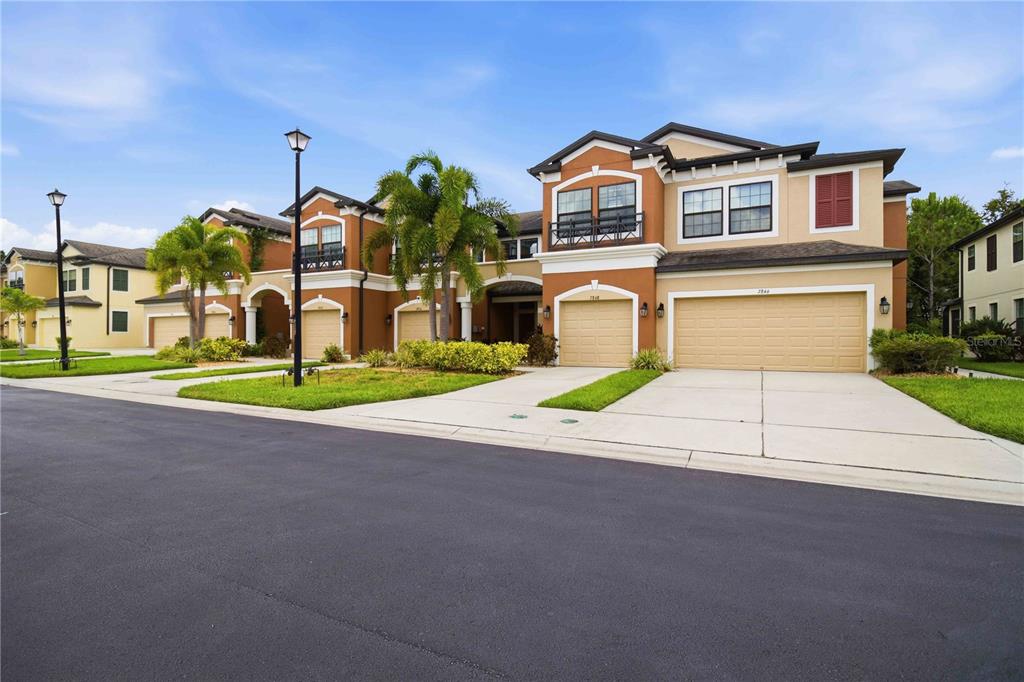 A row of multi-story townhomes with tan stucco walls, tile roofs, and attached garages — 7856 52ND TERRACE E, BRADENTON, FL