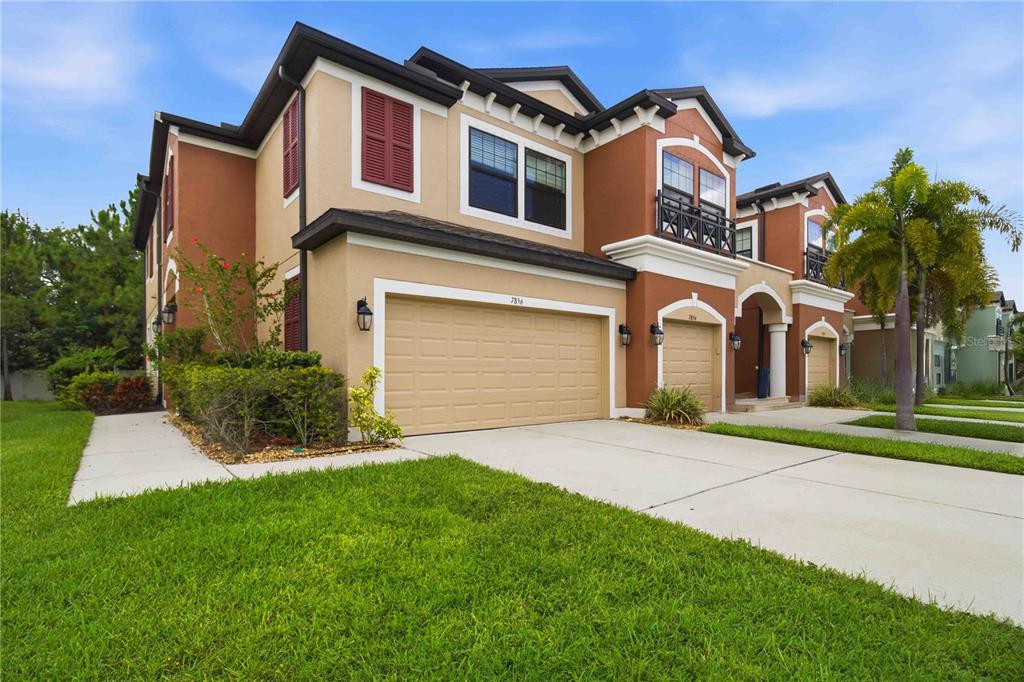 A two-story suburban house features a tan stucco exterior, a two-car garage, and red shutters — 7856 52ND TERRACE E, BRADENTON, FL