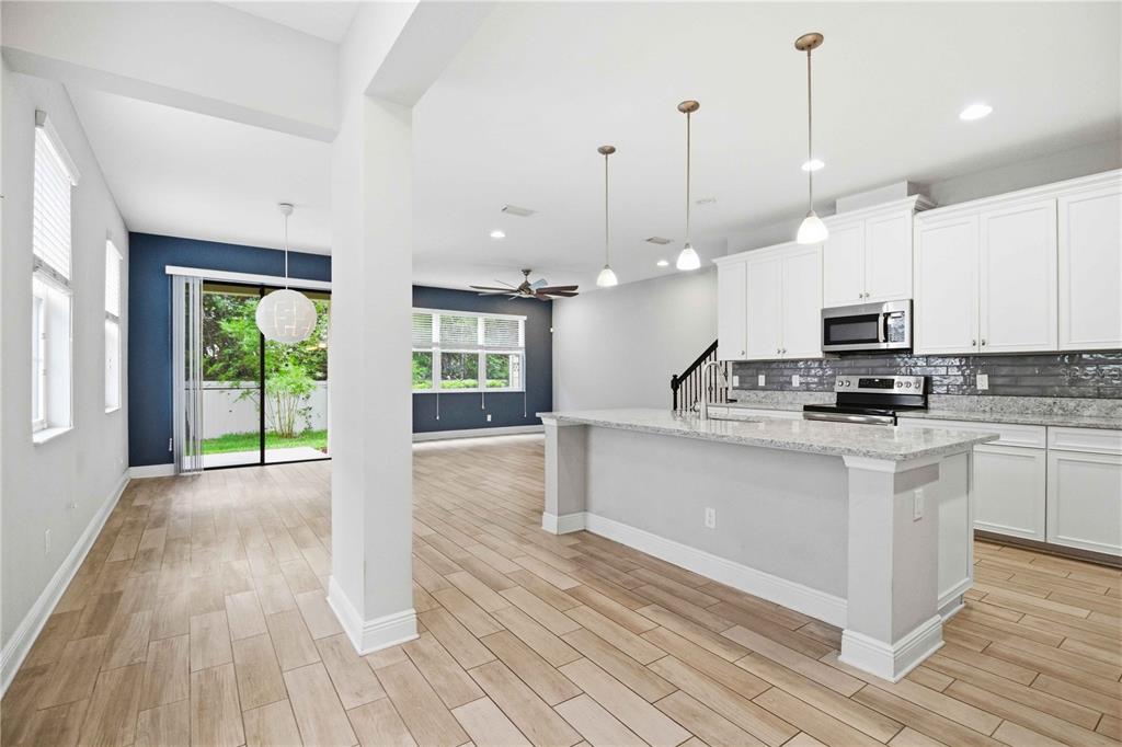 A modern kitchen with white cabinets and a granite island overlooks an open living area — 7856 52ND TERRACE E, BRADENTON, FL