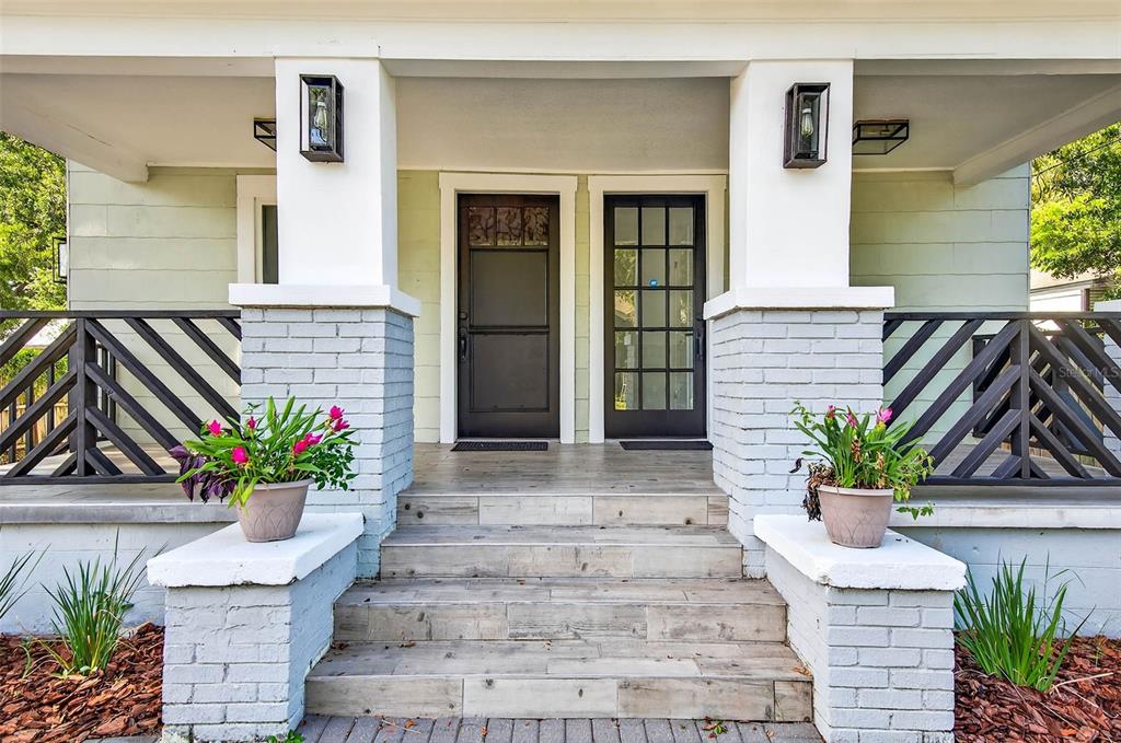 A front porch with two doors, brick columns, and potted plants on a light-colored house — 809 E BAKER STREET UNIT A, TAMPA, FL