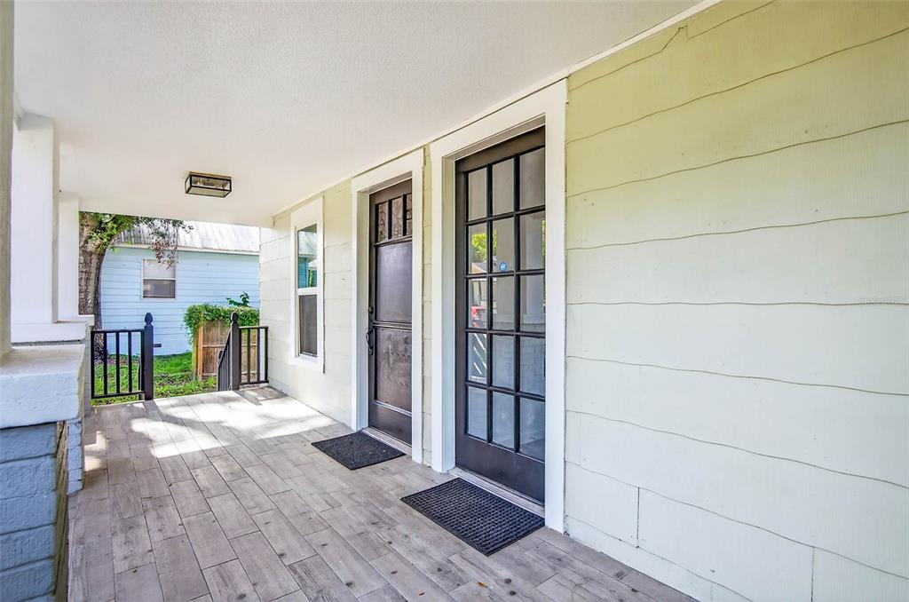 A covered front porch features light-colored wood-look tile flooring and two dark-framed glass doors — 809 E BAKER STREET UNIT A, TAMPA, FL