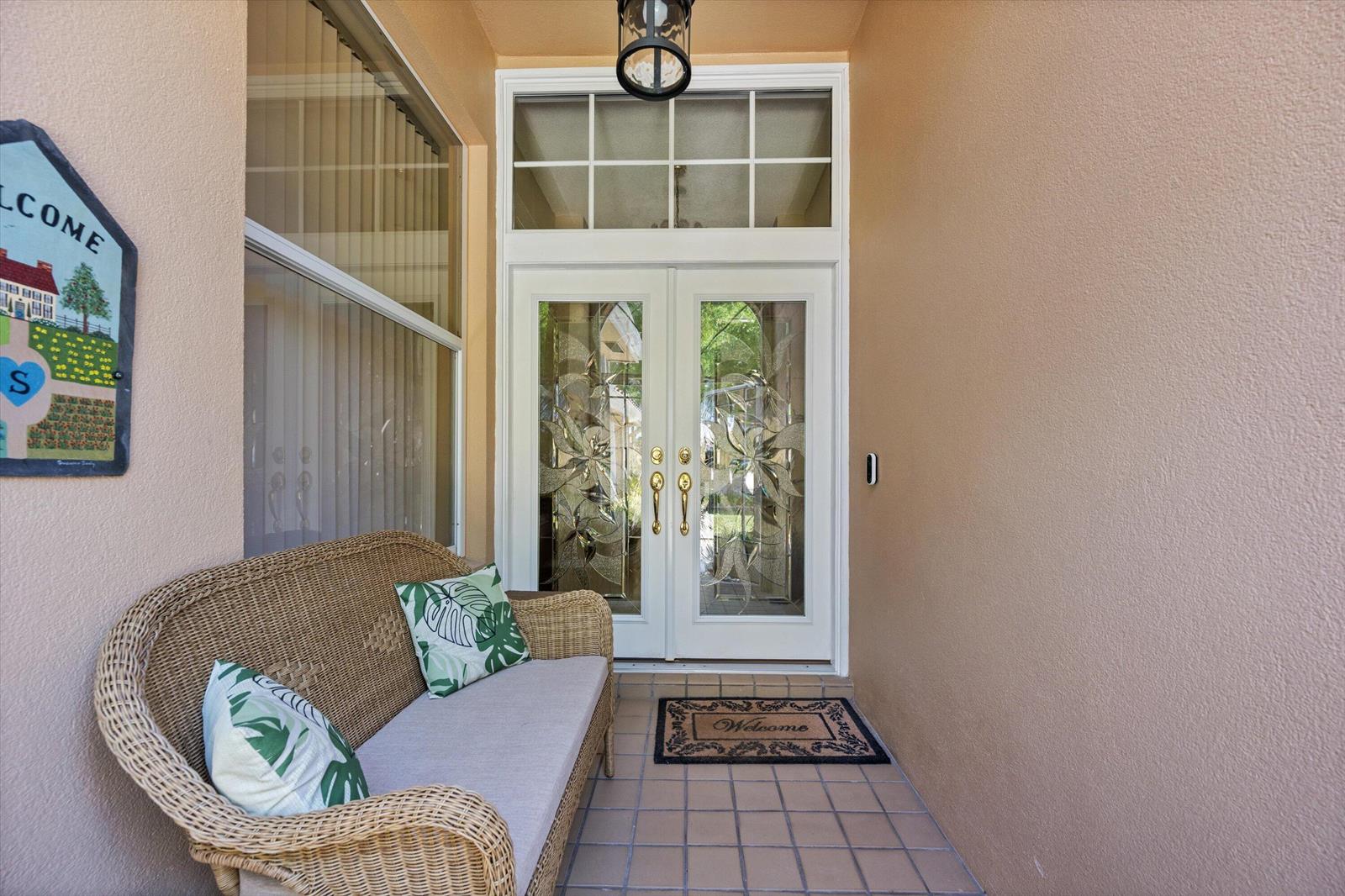 A covered entryway features a wicker bench, a welcome mat, and double glass-paneled doors — 178 Hampton Place, Jupiter FL 33458, JUPITER, FL