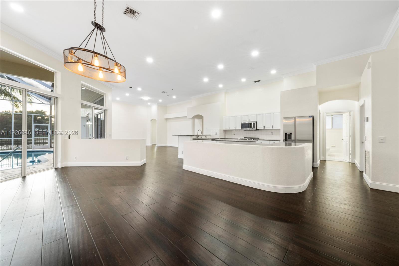 An open-concept kitchen and living area features dark wood flooring, white cabinetry, and pool access — 2893 Oakbrook Dr, Weston FL 33332, WESTON, FL