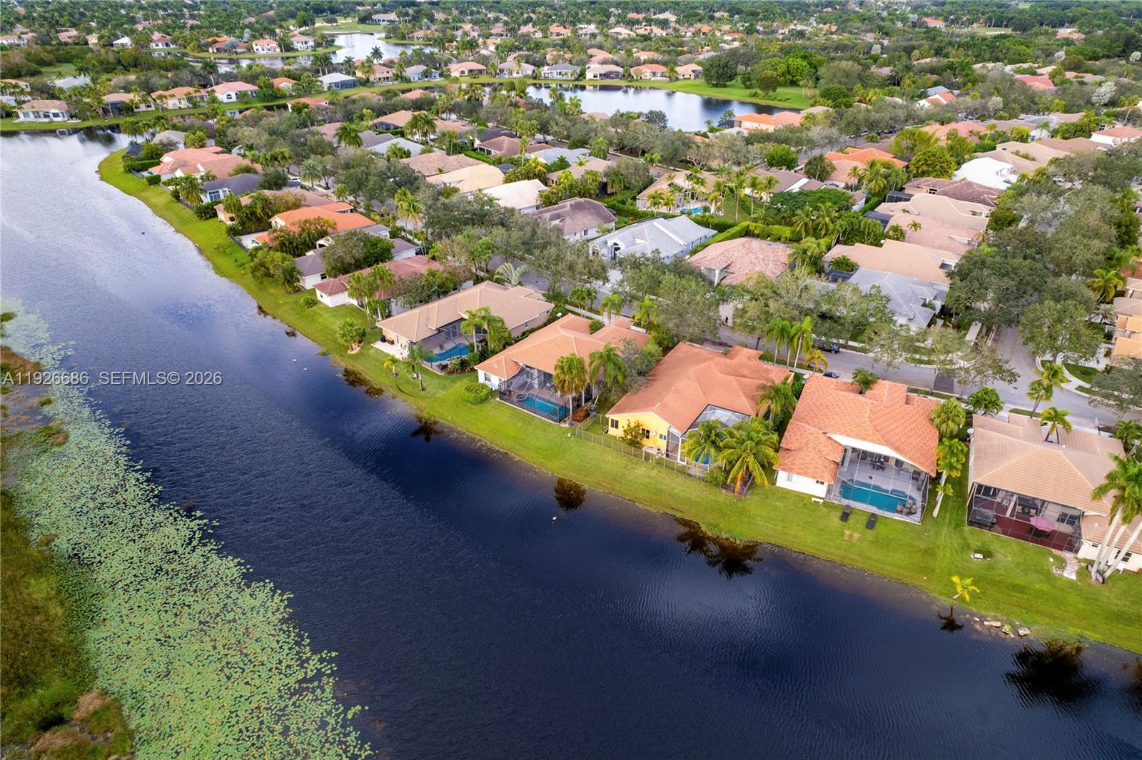 An aerial view shows several suburban houses with swimming pools situated along a large lake — 2893 Oakbrook Dr, Weston FL 33332, WESTON, FL