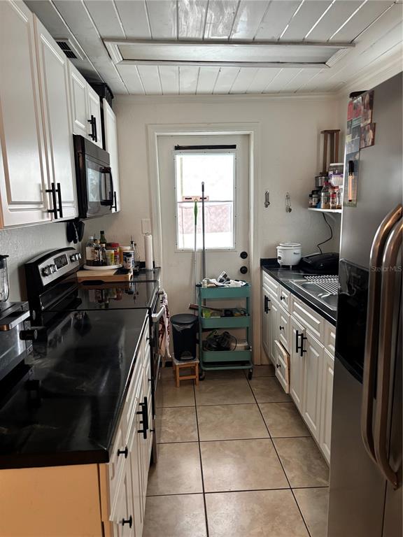 A galley kitchen features white cabinets, black appliances, tile flooring, and a rear exterior door — 2440 WEBER STREET, LAKELAND, FL