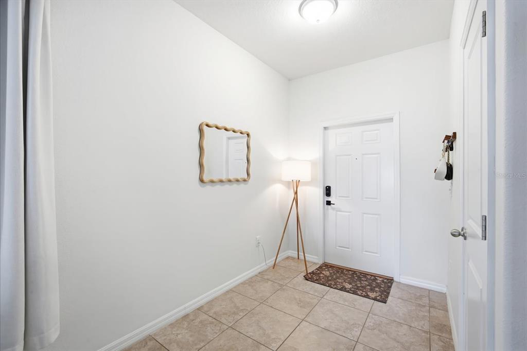 An entryway features white walls, tile flooring, a tripod floor lamp, and a wall mirror — 7656 GINGER LILY COURT, TAMPA, FL
