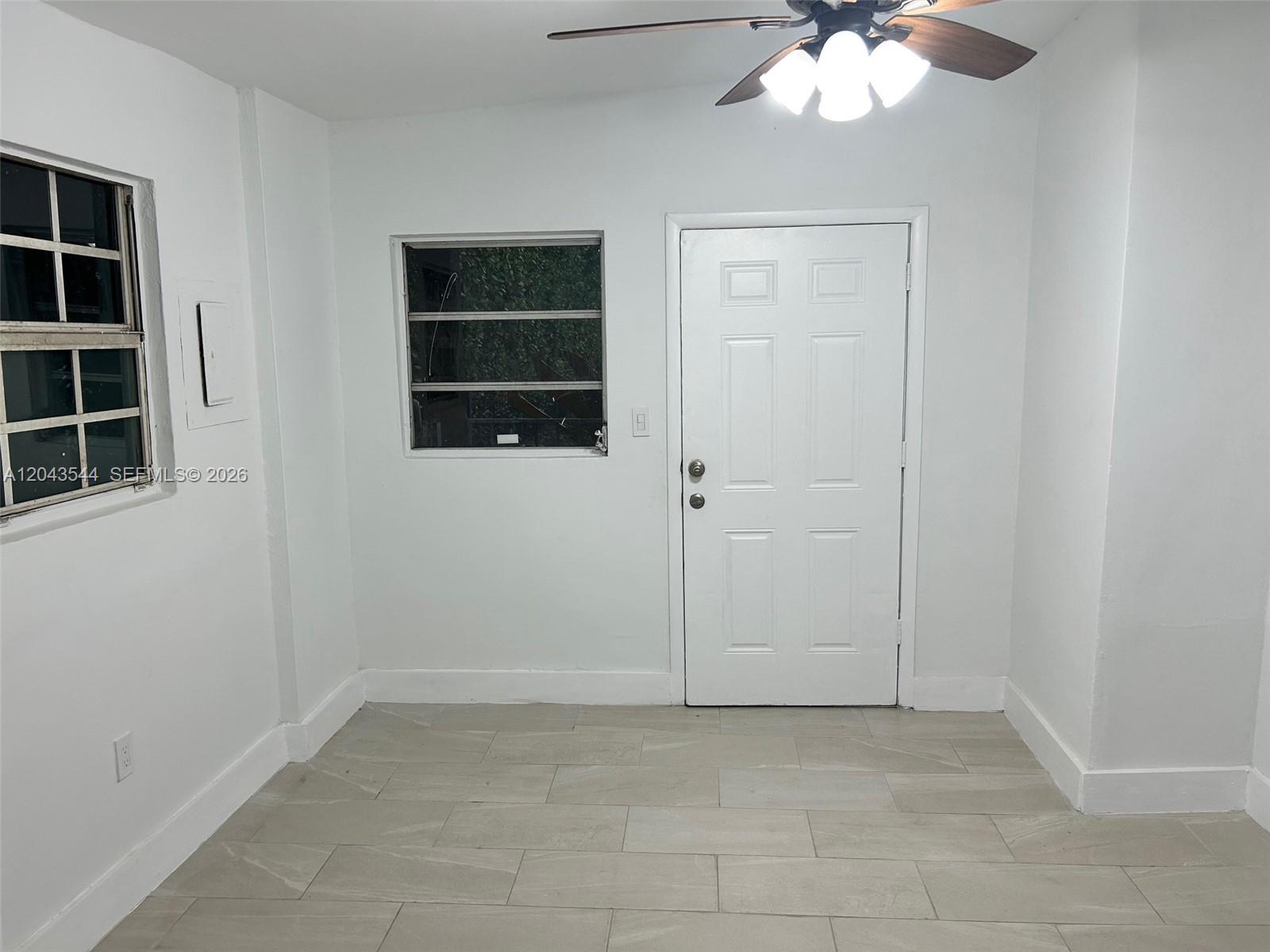 A room with white walls, tile flooring, a ceiling fan, two windows, and a door — 261 NW 49th St # C, Miami FL 33127, MIAMI, FL