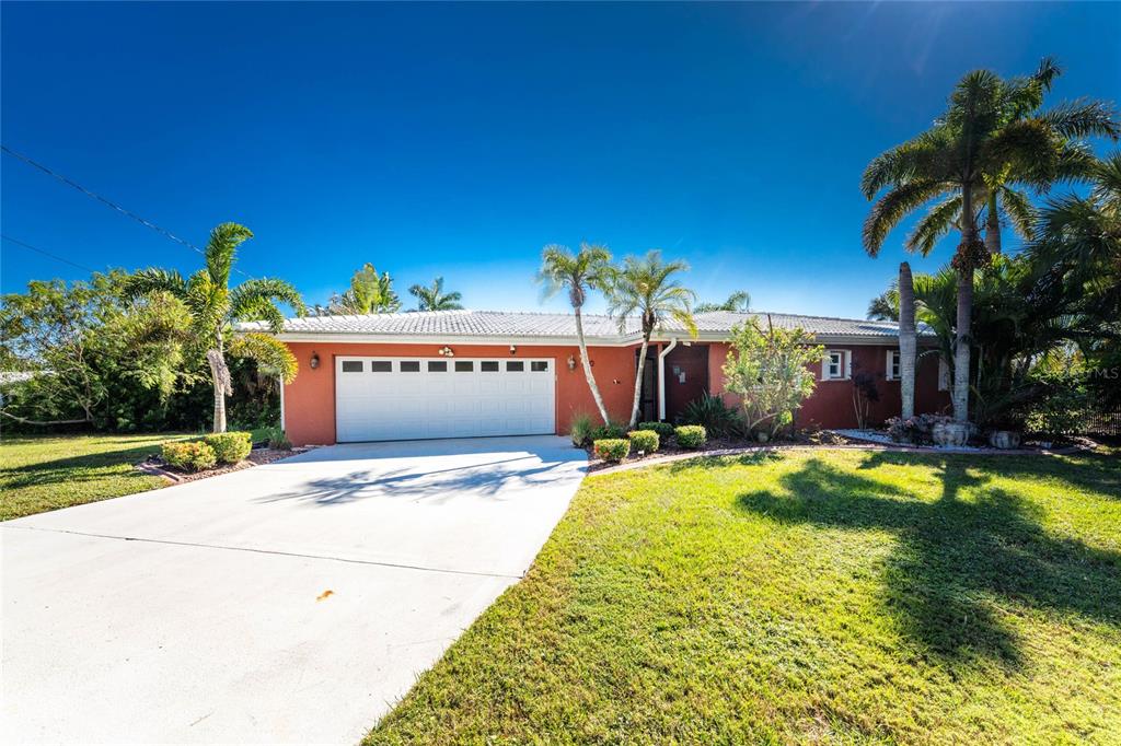 A single-story house with a terracotta exterior, white garage door, and palm trees in front — 180 PURDY DRIVE, PUNTA GORDA, FL