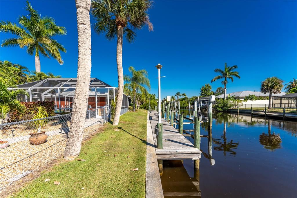 A wooden boat dock extends into a canal beside a house with a screened patio — 180 PURDY DRIVE, PUNTA GORDA, FL
