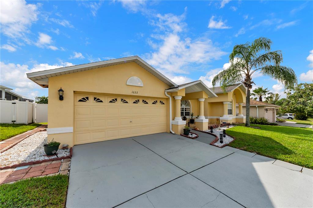 A yellow single-story house with a two-car garage, a palm tree, and a concrete driveway — 1622 CRAZY HORSE DR, LUTZ, FL