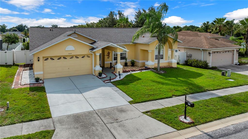 A yellow single-story house with a two-car garage, a palm tree, and a green lawn — 1622 CRAZY HORSE DR, LUTZ, FL