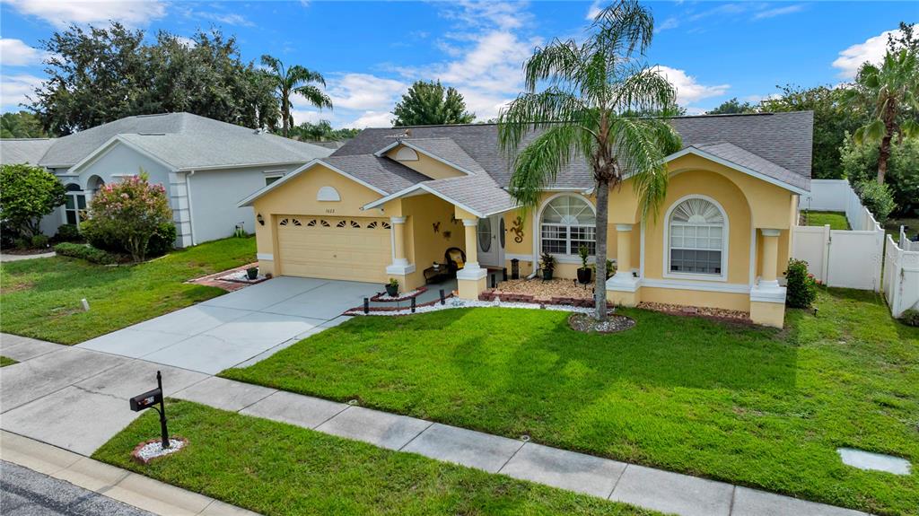 A yellow single-story house with a two-car garage, a palm tree, and a green lawn — 1622 CRAZY HORSE DR, LUTZ, FL