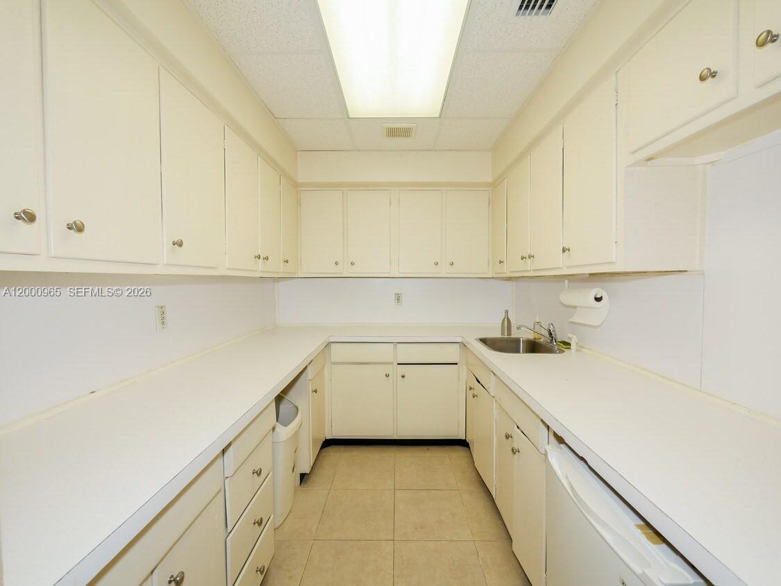 A galley-style kitchen features white cabinets, white countertops, and light-colored floor tiles — 3113 Ponce De Leon Blvd, Coral Gables FL 33134, CORAL GABLES, FL
