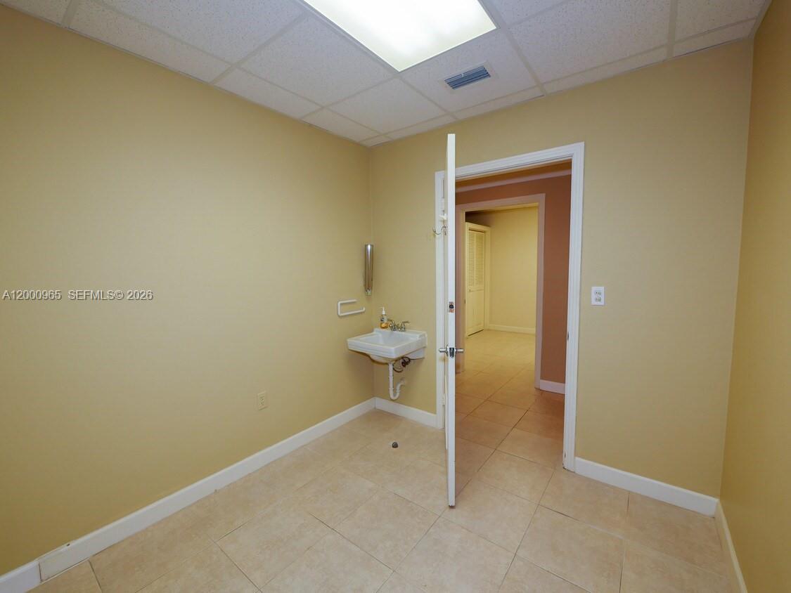 A small room with beige walls, tile flooring, a wall-mounted sink, and an open doorway — 3113 Ponce De Leon Blvd, Coral Gables FL 33134, CORAL GABLES, FL