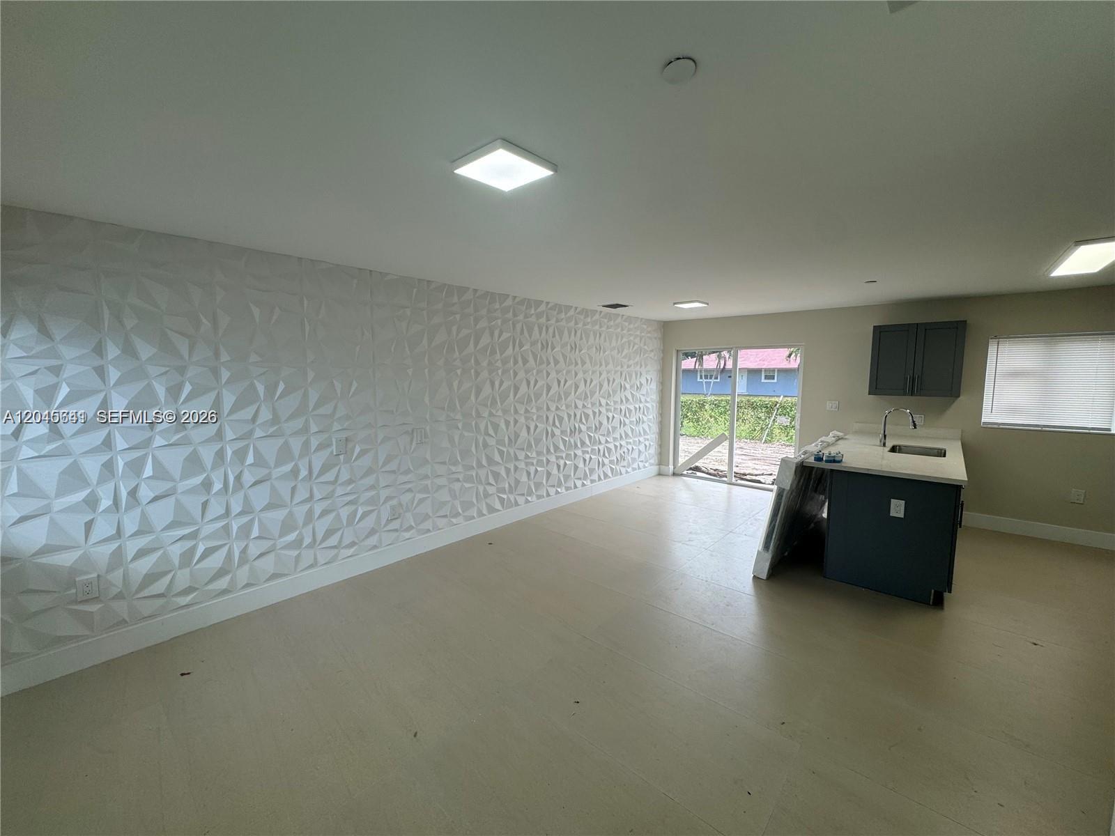 An open-concept room features a textured accent wall, light flooring, and a small kitchen island — 205 NW 159th St, Miami FL 33169, MIAMI, FL