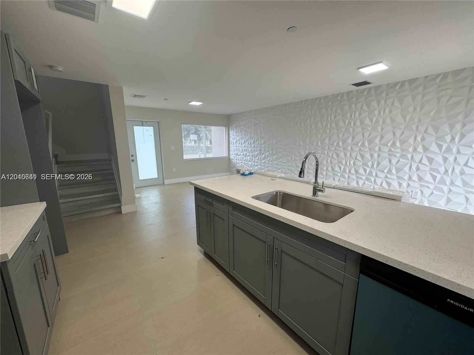 A kitchen features a gray island with a sink and a textured white accent wall — 205 NW 159th St, Miami FL 33169, MIAMI, FL