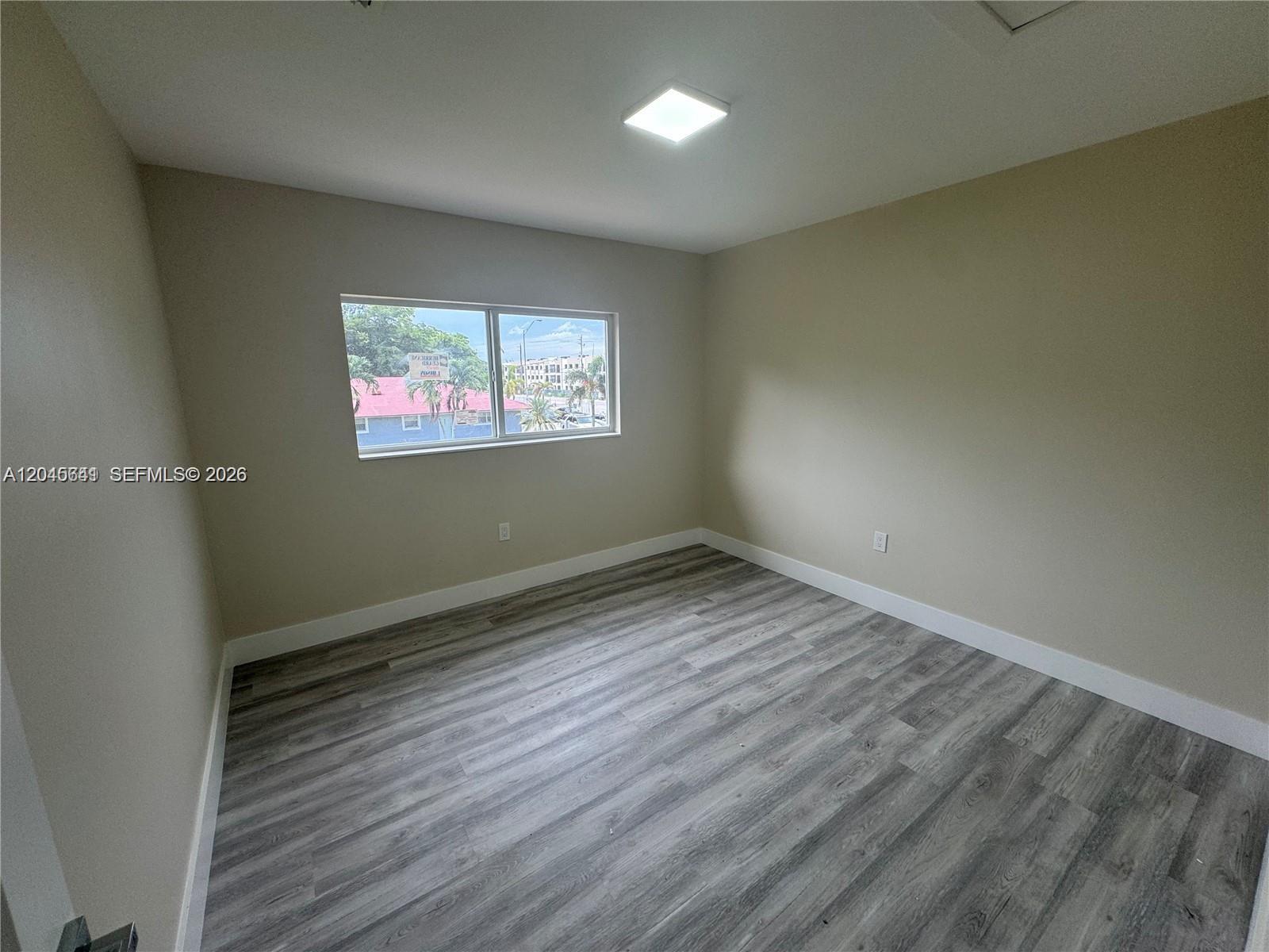 An empty bedroom features light-colored walls, a single window, and grey wood-look flooring — 205 NW 159th St, Miami FL 33169, MIAMI, FL
