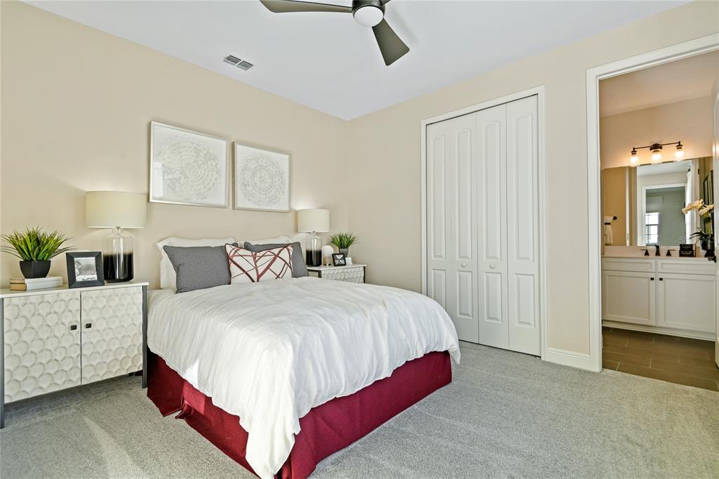 A bedroom with a bed, white closet doors, and an attached bathroom with a vanity — 5110 KINSLEY DRIVE, WINTER HAVEN, FL