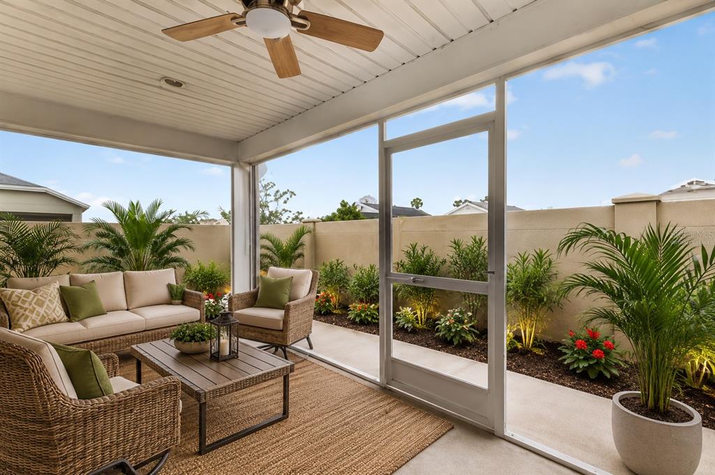 A screened-in patio features wicker furniture, a ceiling fan, and a landscaped garden area — 1674 CADORETTE DRIVE, THE VILLAGES, FL