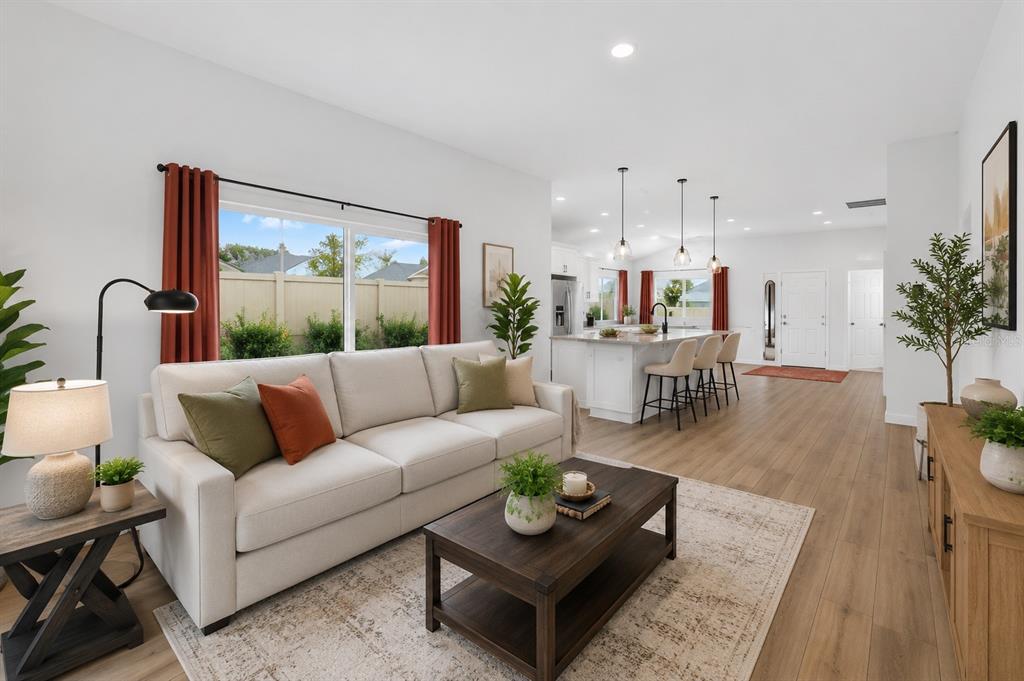 A bright living room with a beige sofa opens into a kitchen with an island — 1674 CADORETTE DRIVE, THE VILLAGES, FL