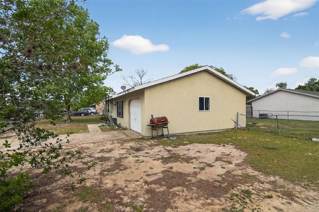 A side view of a single-story house with a garage, a grill, and a fenced yard — 8779 SE 89TH PLACE, OCALA, FL