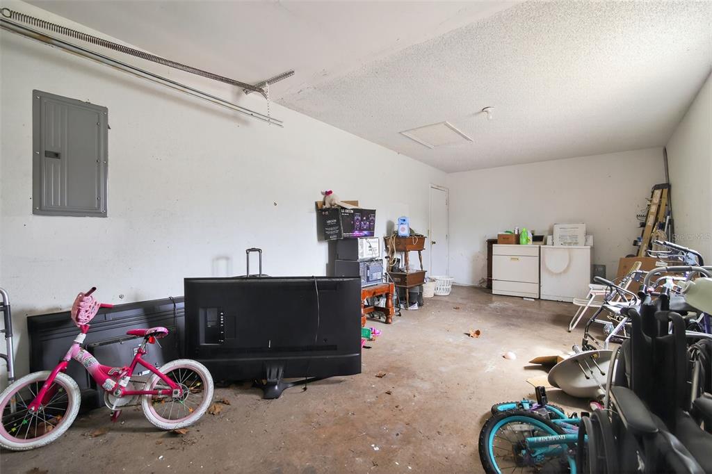 A cluttered garage with concrete floors, a pink bicycle, and various household items stored inside — 8779 SE 89TH PLACE, OCALA, FL