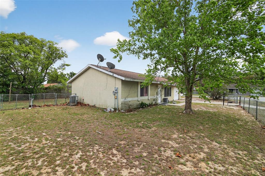 A side view of a single-story house with a large tree and a fenced yard — 8779 SE 89TH PLACE, OCALA, FL